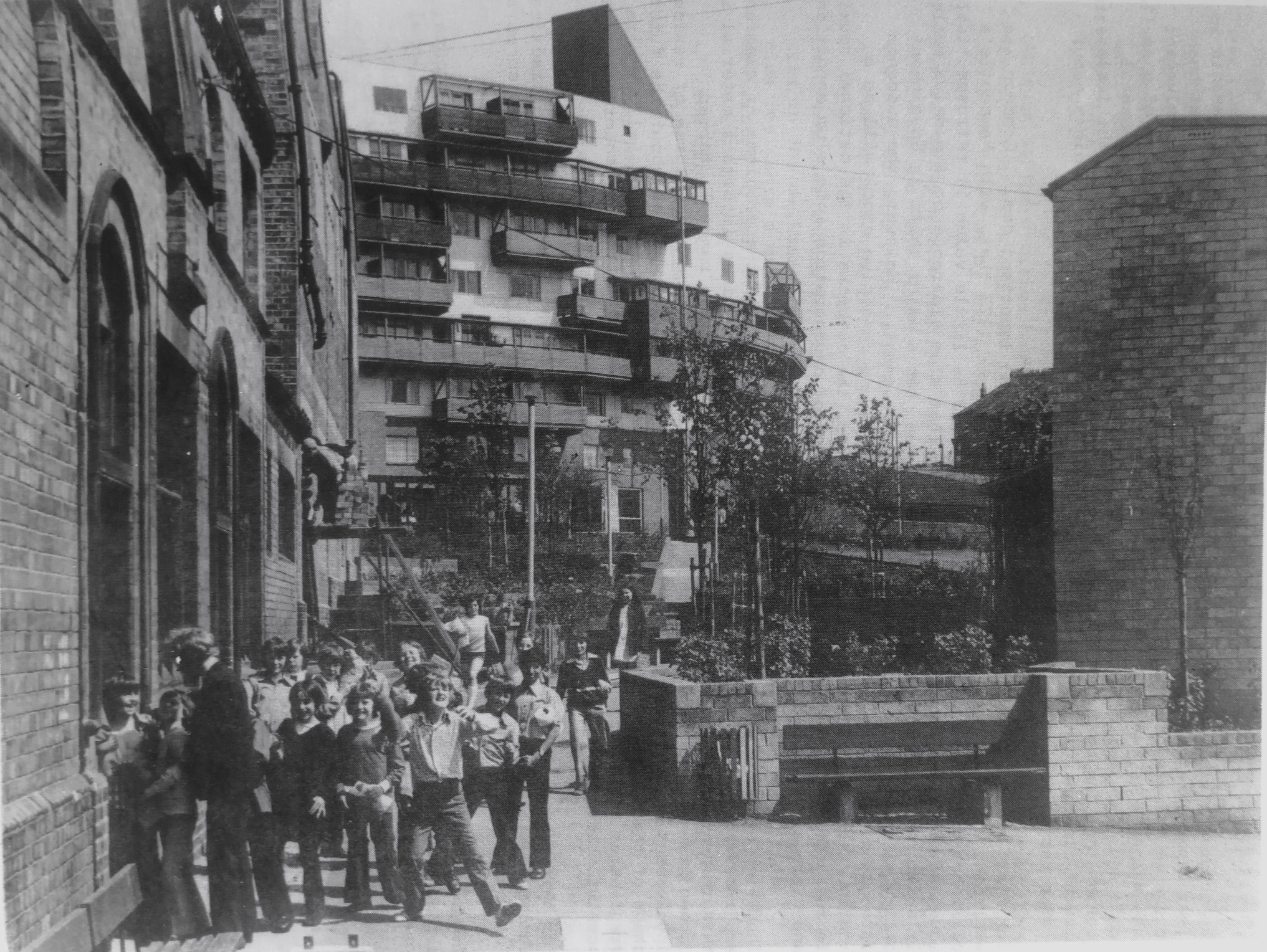 A group of children and an adult stand in front of the Byker Wall