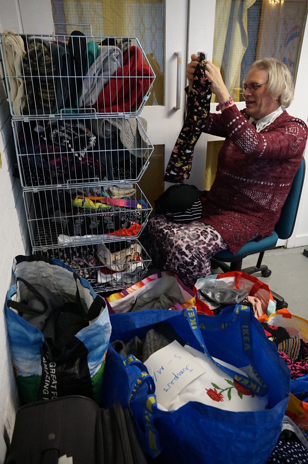 A volunteer sits on a chair folding clothing from a large pile