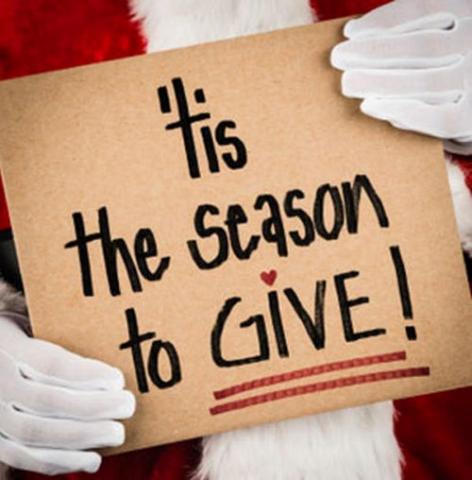 Santa holds a sign reading tis the season to give!