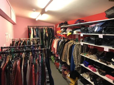 A small colourful room is packed from floor to ceiling with shelves and rails of clothes