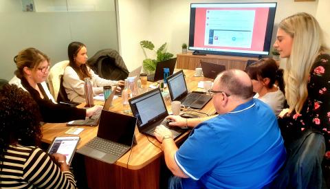 A small group of people sit around a table with laptops